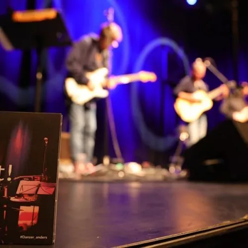 Die CD "Jetzt!" am Bühnenrand mit der Band unscharf im Hintergrund.