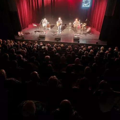 Totale der Bühne mit Zuschauern im Vordergrund und Bühne und Band im Hintergrund.