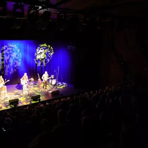 Totale auf Band und Bühne vom hinteres Saalende mit bunten Lichtornamenten.