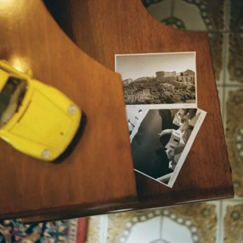 Detailaufnahme mit gelbem Spielzeug-Porsche und Griechenland-Fotos.