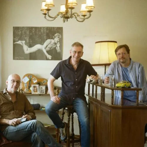 Die Träumer an einer Bar in einem Wohnzimmer. Im Hintergrund ein Bild von Georg Danzer.