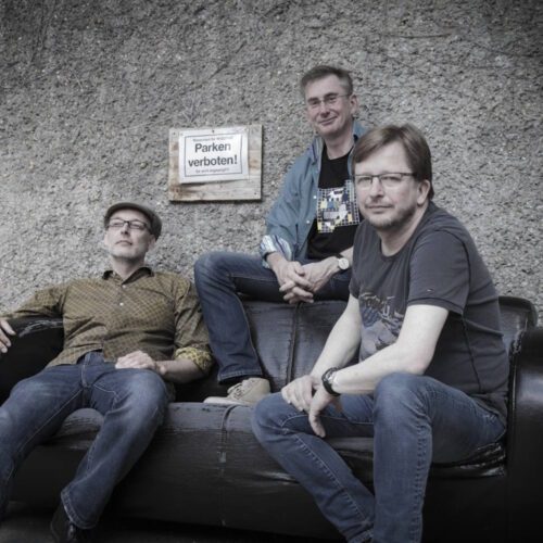 Träumer Band-Foto: Die drei Musiker vor einer Betonwand auf einem Ledersofa