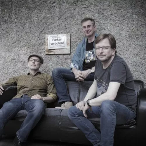 Träumer Band-Foto: Die drei Musiker vor einer Betonwand auf einem Ledersofa