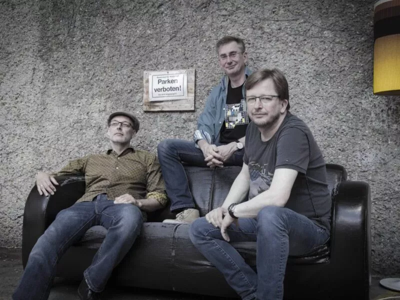 Träumer Band-Foto: Die drei Musiker vor einer Betonwand auf einem Ledersofa