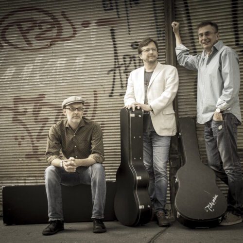 Träumer Band-Foto: Die drei Musiker mit Gitarrenkoffern vor einem geschlossenen Rollladen