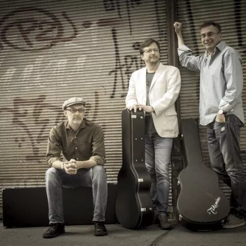 Träumer Band-Foto: Die drei Musiker mit Gitarrenkoffern vor einem geschlossenen Rollladen